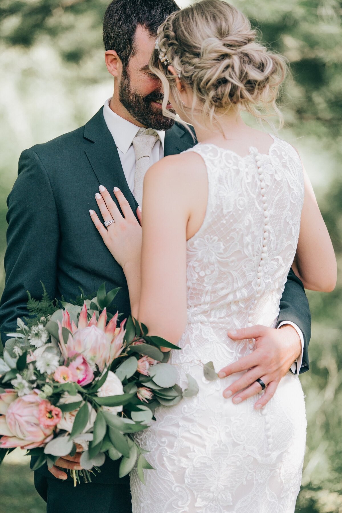 A beautiful detail photo of a bride and groom. The bride is wearing a stunning ivory wedding dress with a lace back and you can see that the groom is holding her whimsical bridal bouquet