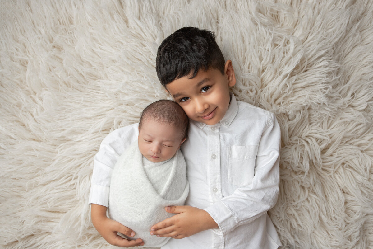 Big brother holding newborn baby brother dressed in white flokati pose