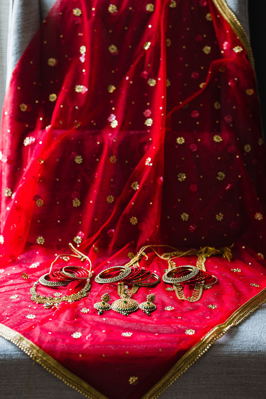 A vibrant red traditional Indian dupatta with golden embroidery and matching jewelry laid out on a fabric surface.