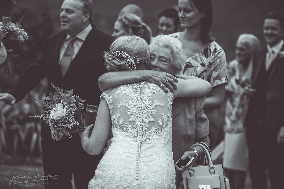A bride is embracing an elderly relative after the wedding ceremony