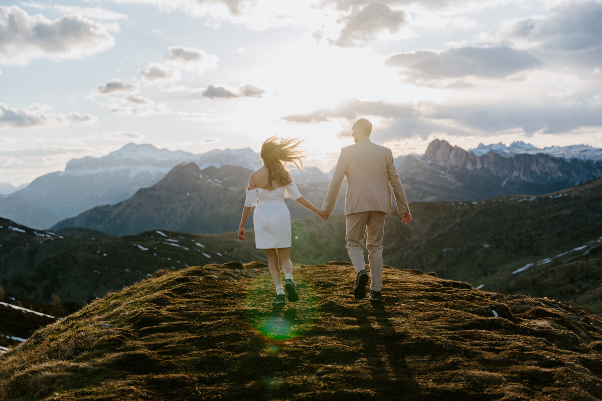 Bride and groom walking hand in hand with dramatic sunset sky