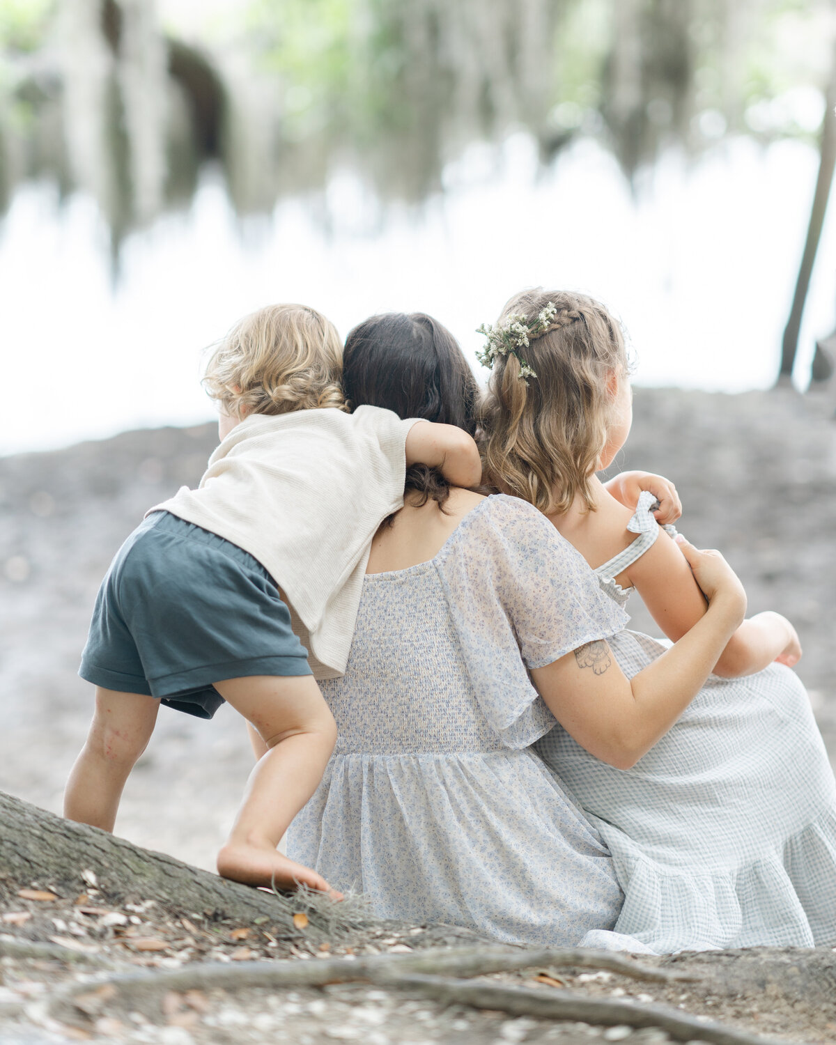 Children cuddling with their mother sitting on the edge of a marsh looking at little crabs by Savannah family photographer Courtney Cronin