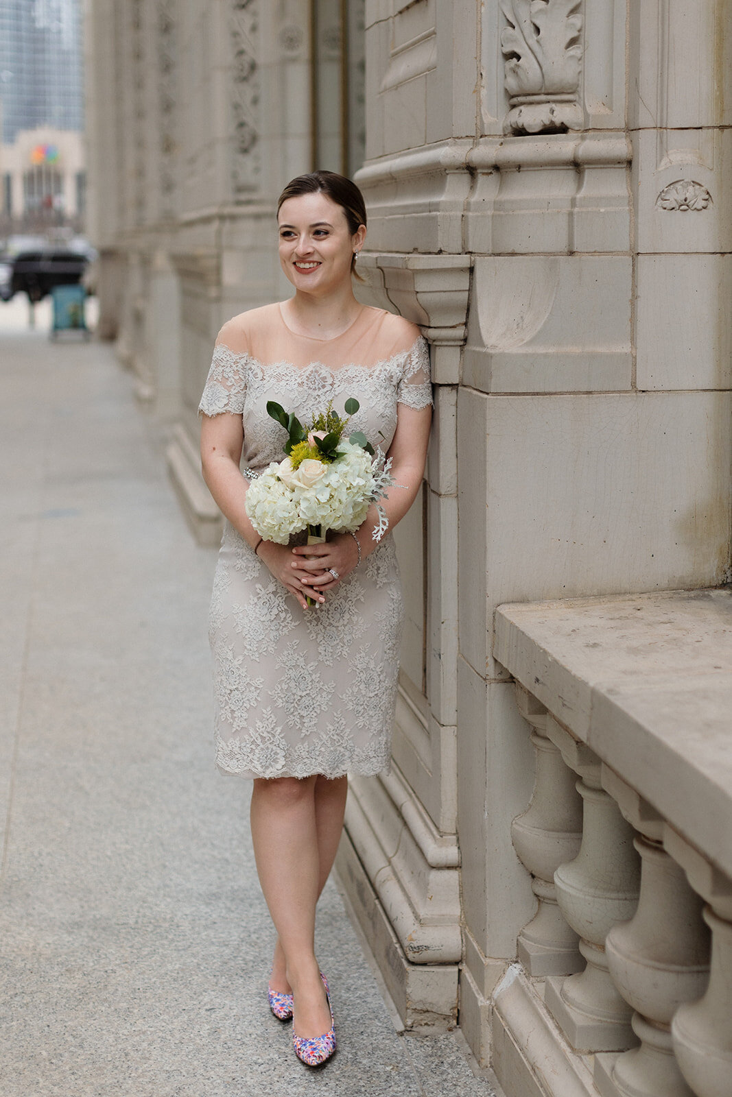 Just Married photo session bride leaning against Wrigley Building in Chicago and holding her bouquet and smiling