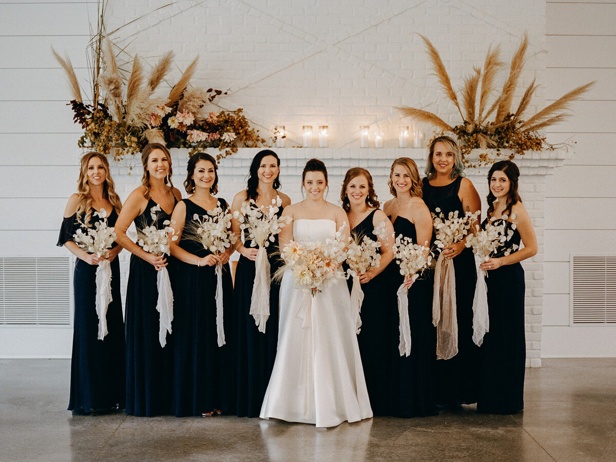 Bridal party standing in front of a fireplace with beautiful floral arrangements at a wedding at the Hutton House in Medicine Lake Minnesota