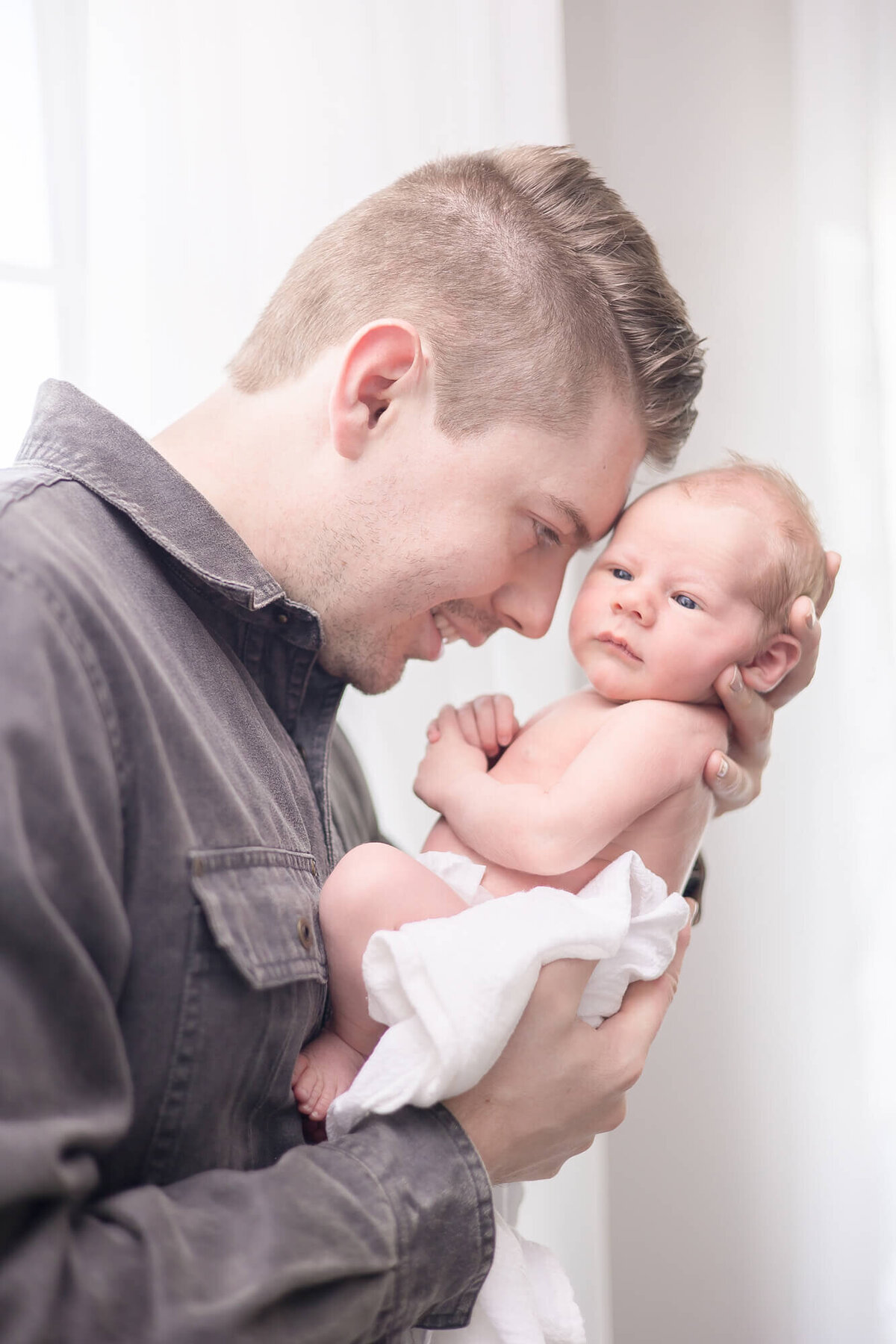 new dad lovingly holding his newborn son up to hisiforehead