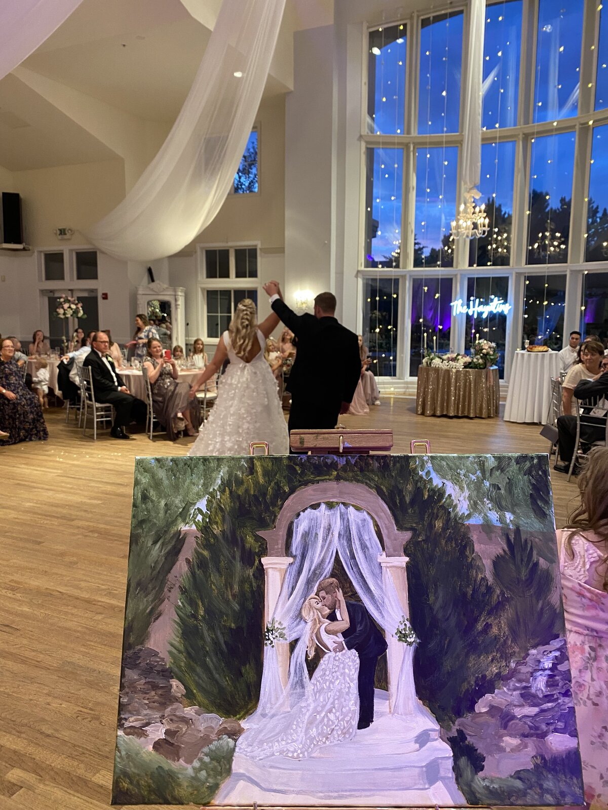 A couple dances during their reception while the artist works on the ceremony painting