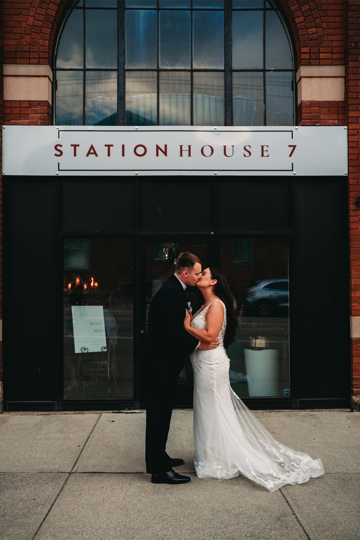 A newlywed couple shares a romantic kiss outside Station House 7 in Pittsburgh, captured in a moody & editorial wedding photography style.