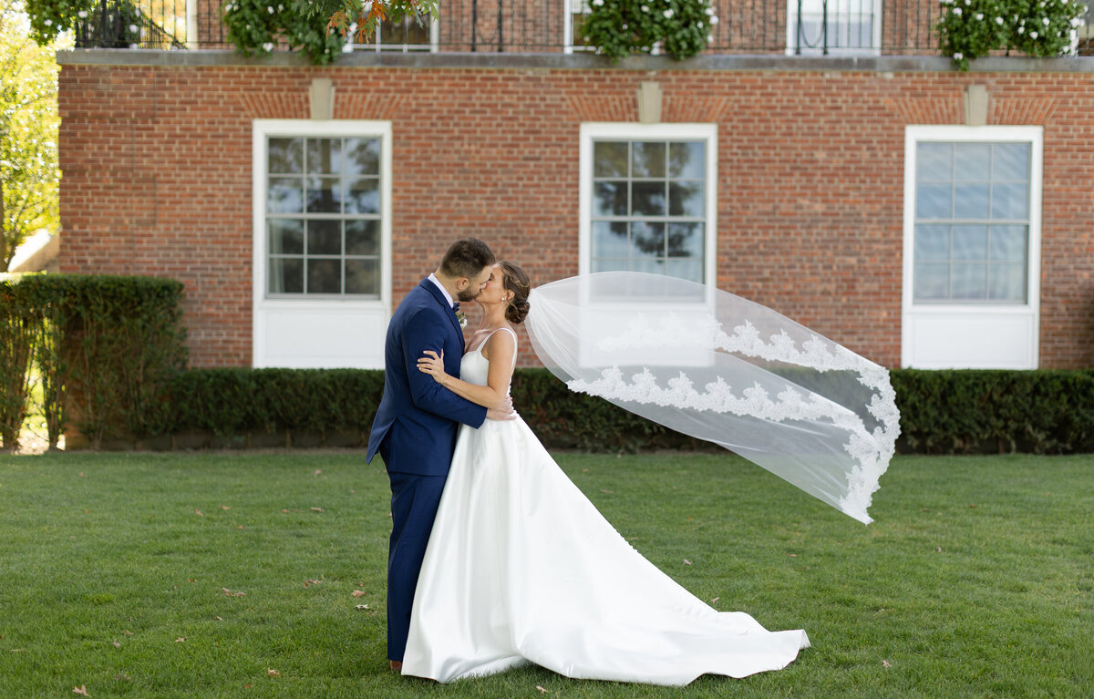 Bride and groom share a kiss as the bride's veil flow dramatically in the wind behind her 