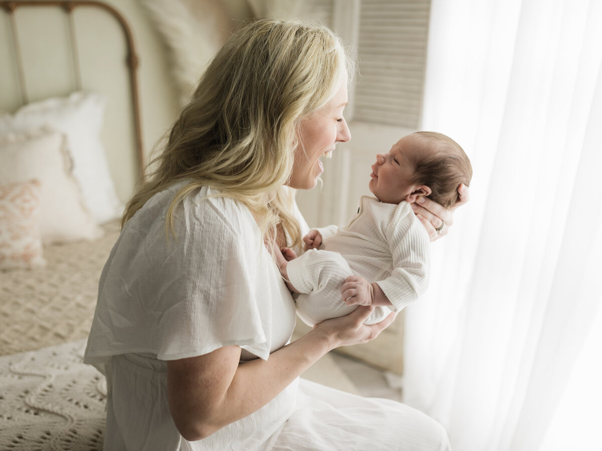 mom holding newborn baby boy in white onesie for studio photoshoot 