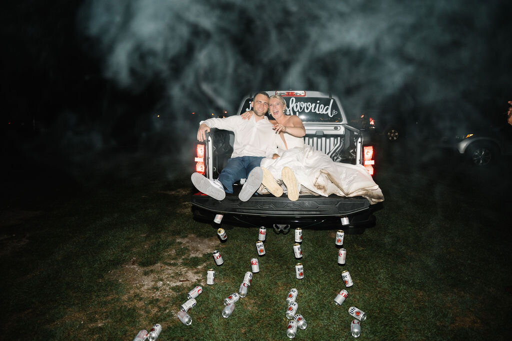 Bride and groom leaving their reception in the back of a truck with cans tied to the back