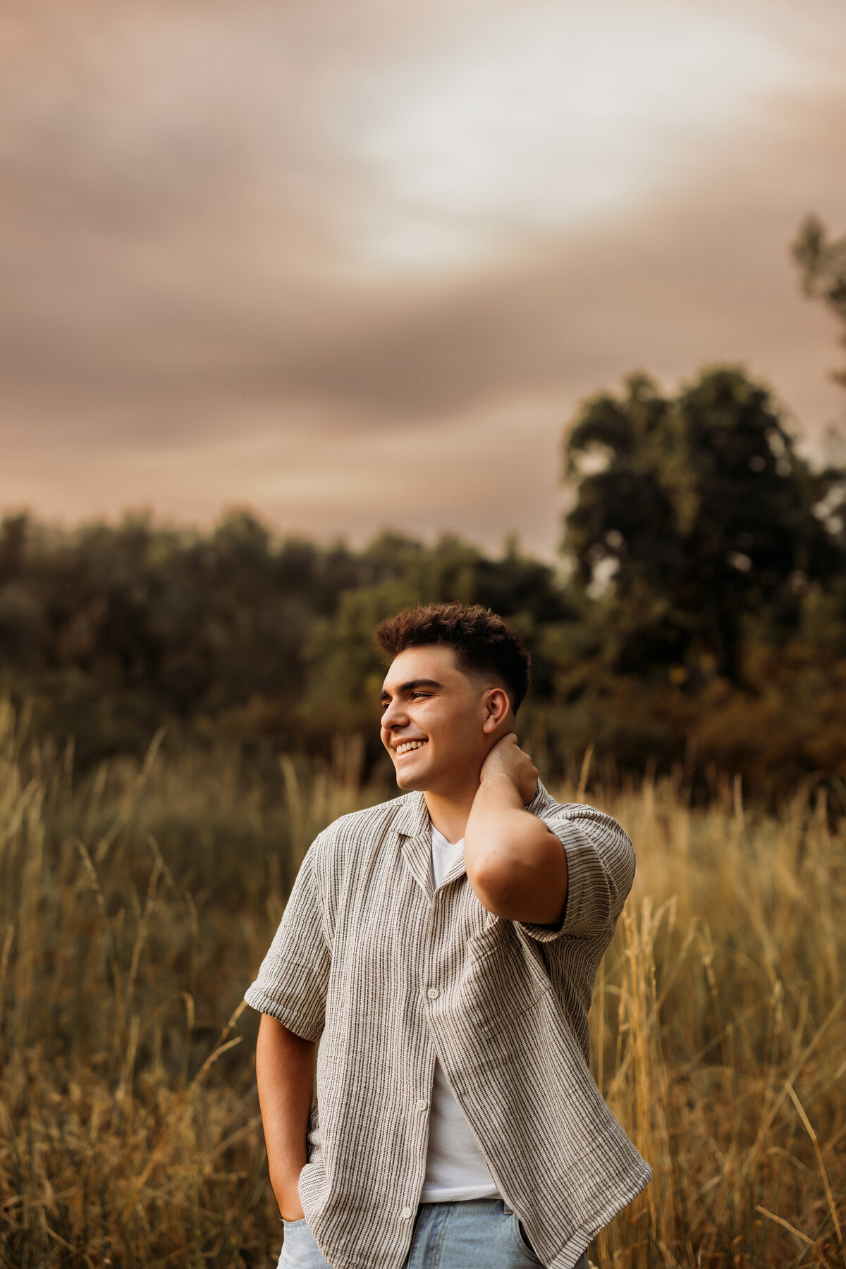 High School senior boy poses and laughs with a natural background with tall grasses for his senior portrait session