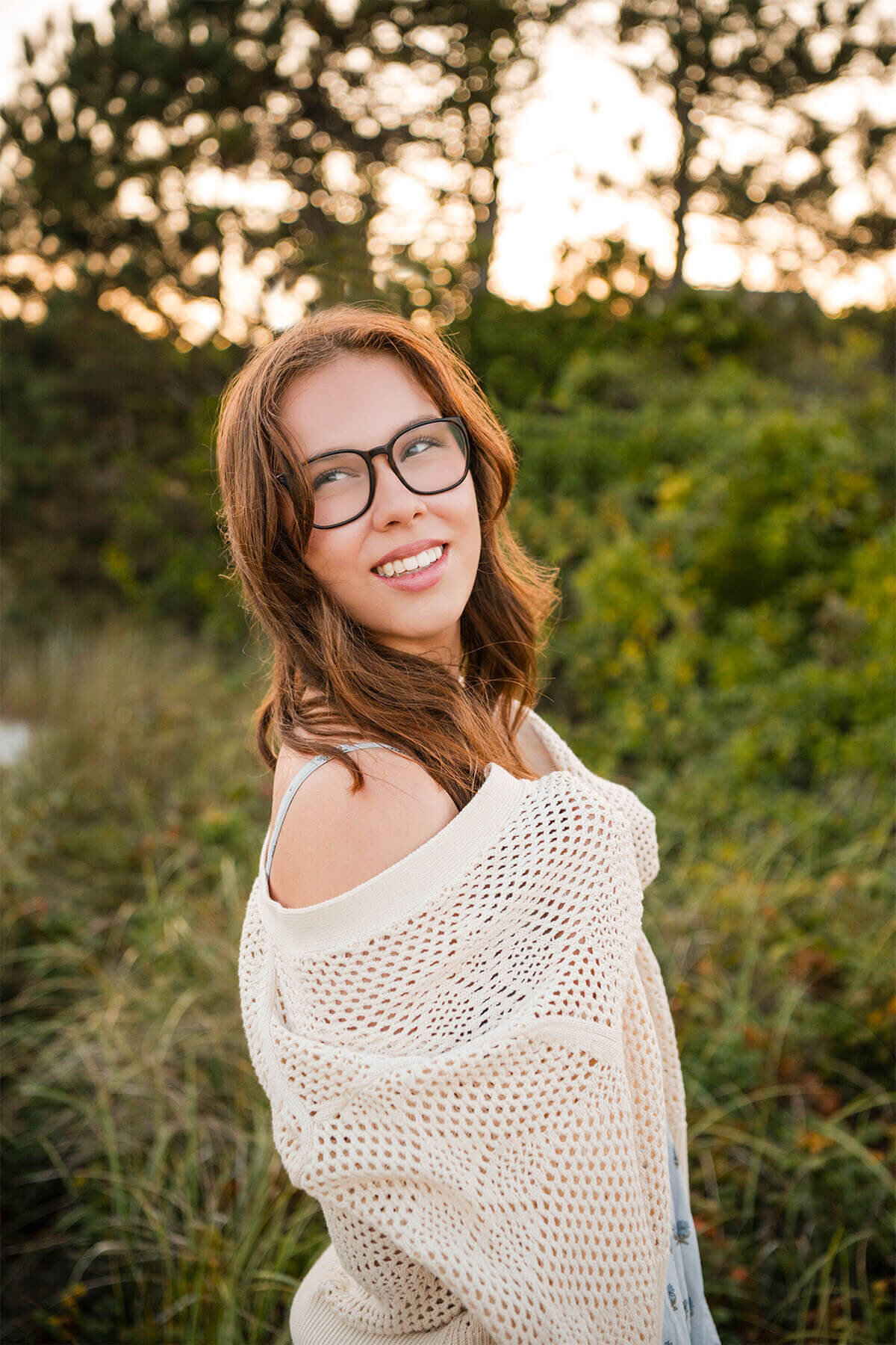 A senior smiles to the side with her sweater draped over her shoulder and the sun hits her head.