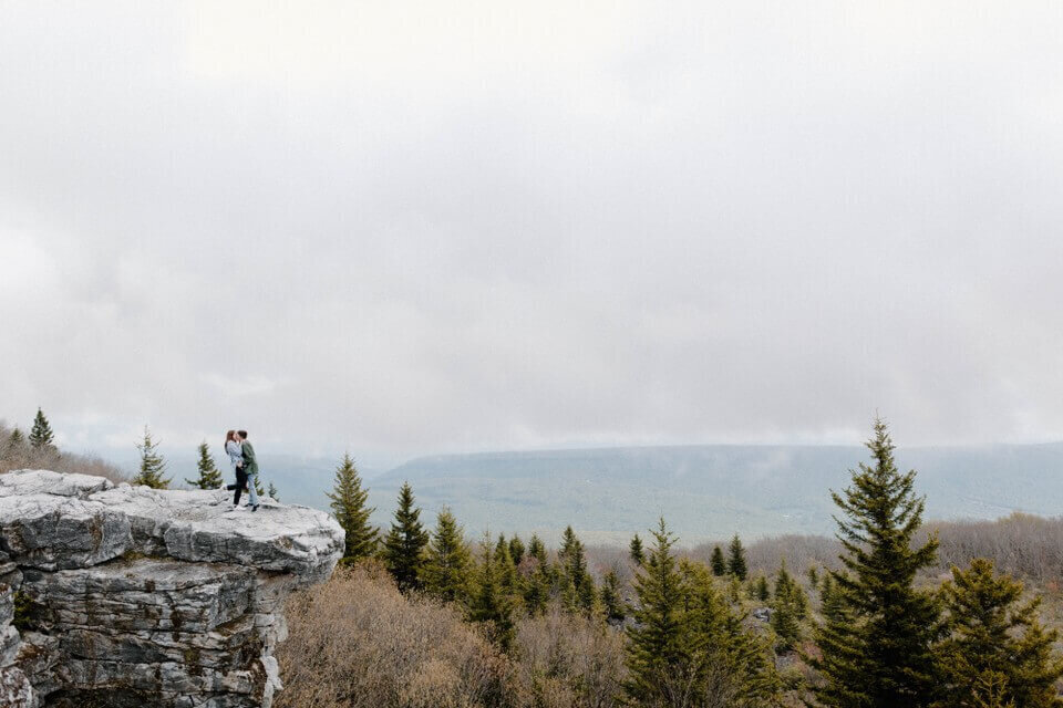 photograph of women kissing on top of beautiful cloudy maryland mountain after rainstorm far shot