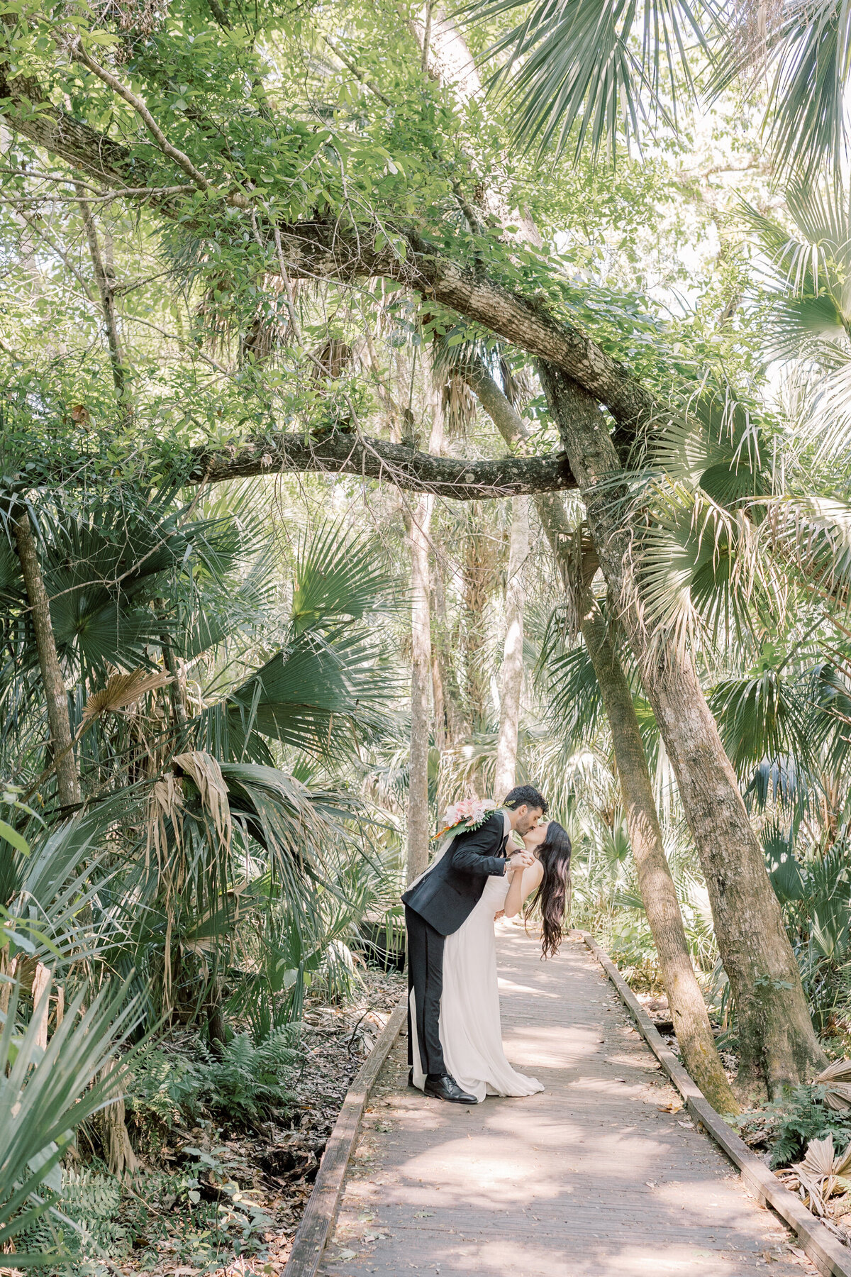 Couple kissing on their elopement day on a boardwalk surrounded by lush green Florida foliage near Apopka.