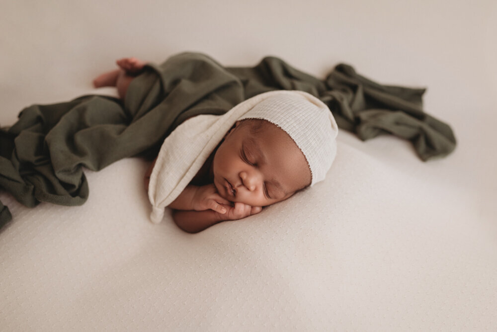 Newborn photos with Atlanta, Georgia newborn photographer of sleeping baby boy with hands under chin draped in olive green fabric with a cream hat on.
