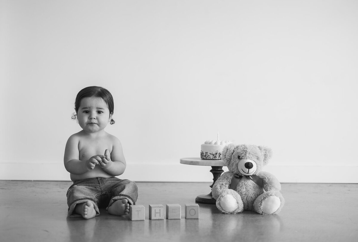 A little boy sits next to cake and a teddy bear.