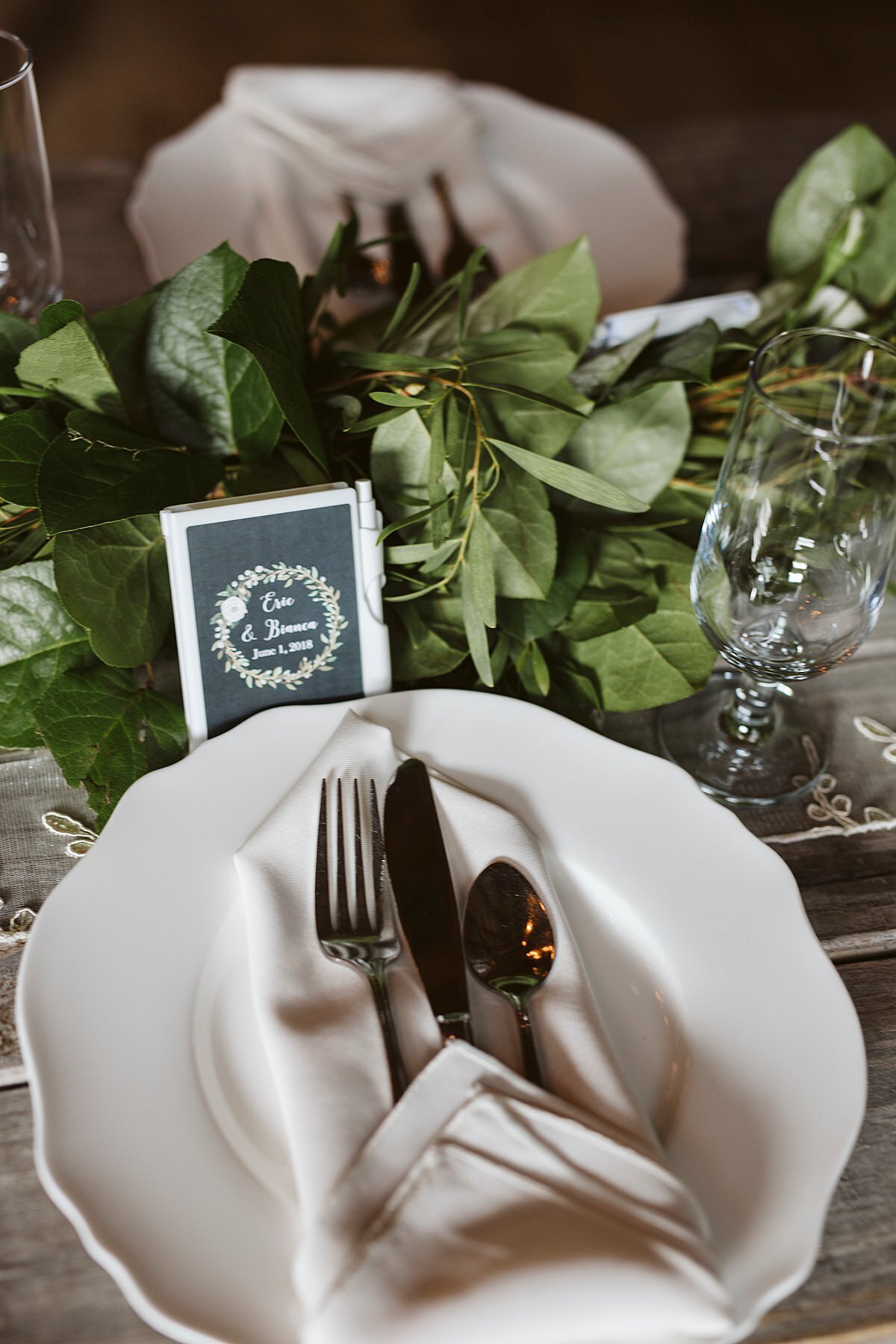 White plate with scalloped edge with a chevron folded napkin and silverware. A long garland of greenery sits on a gray farm table above the plate at Arrington Vineyard.