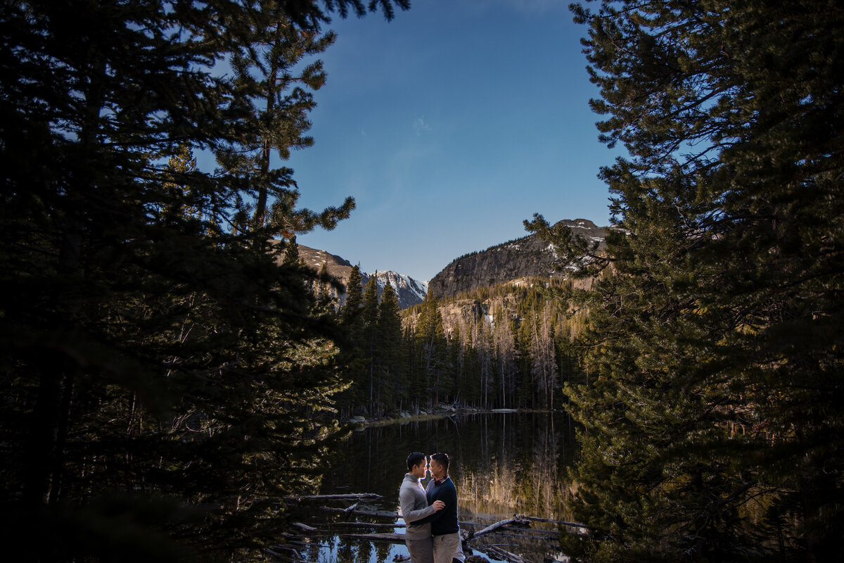 A couple kissing while standing at the edge of a mountain lake.