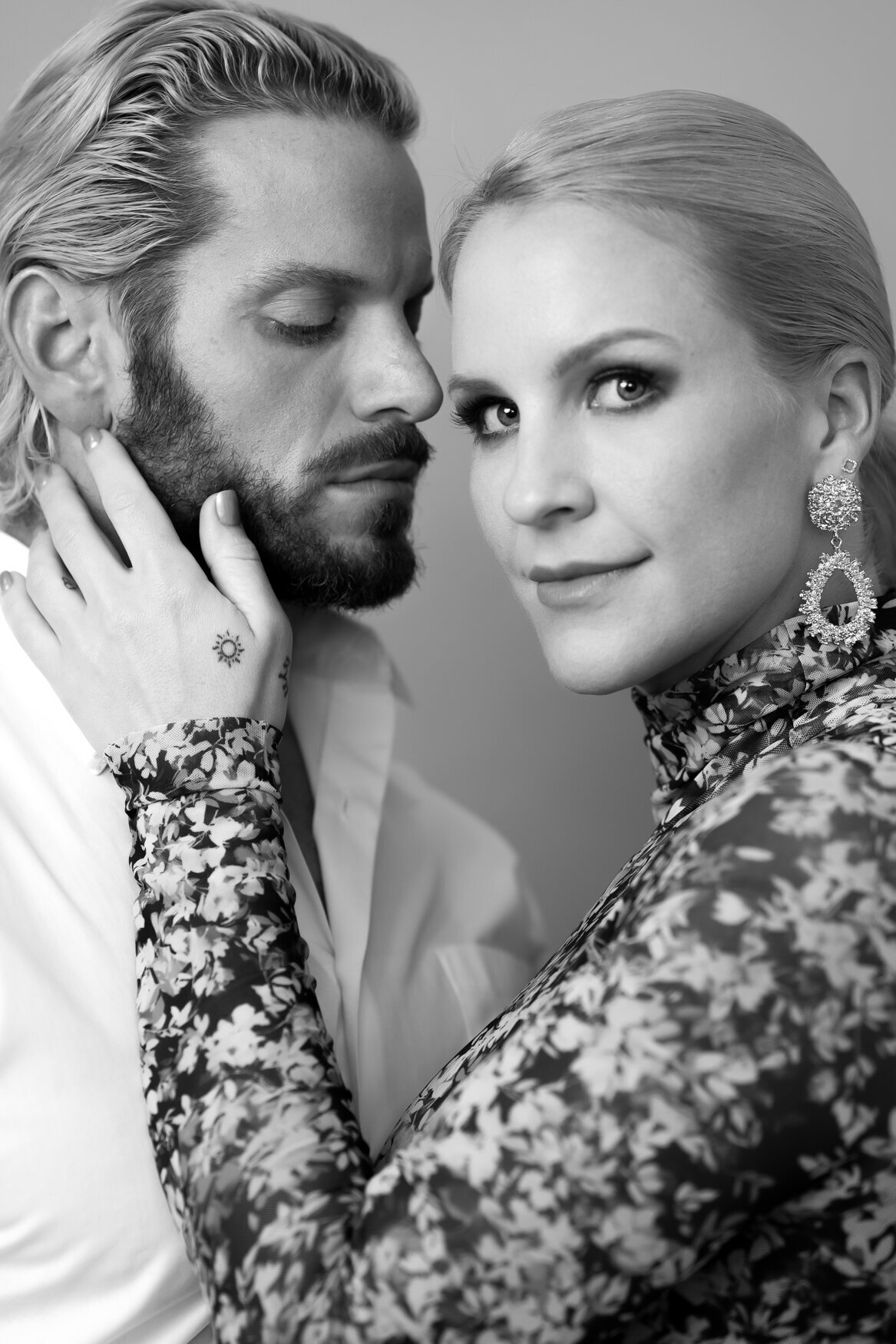 portrait of a couple. the man is looking at the woman and she is looking at the camera while grabbing her partners face