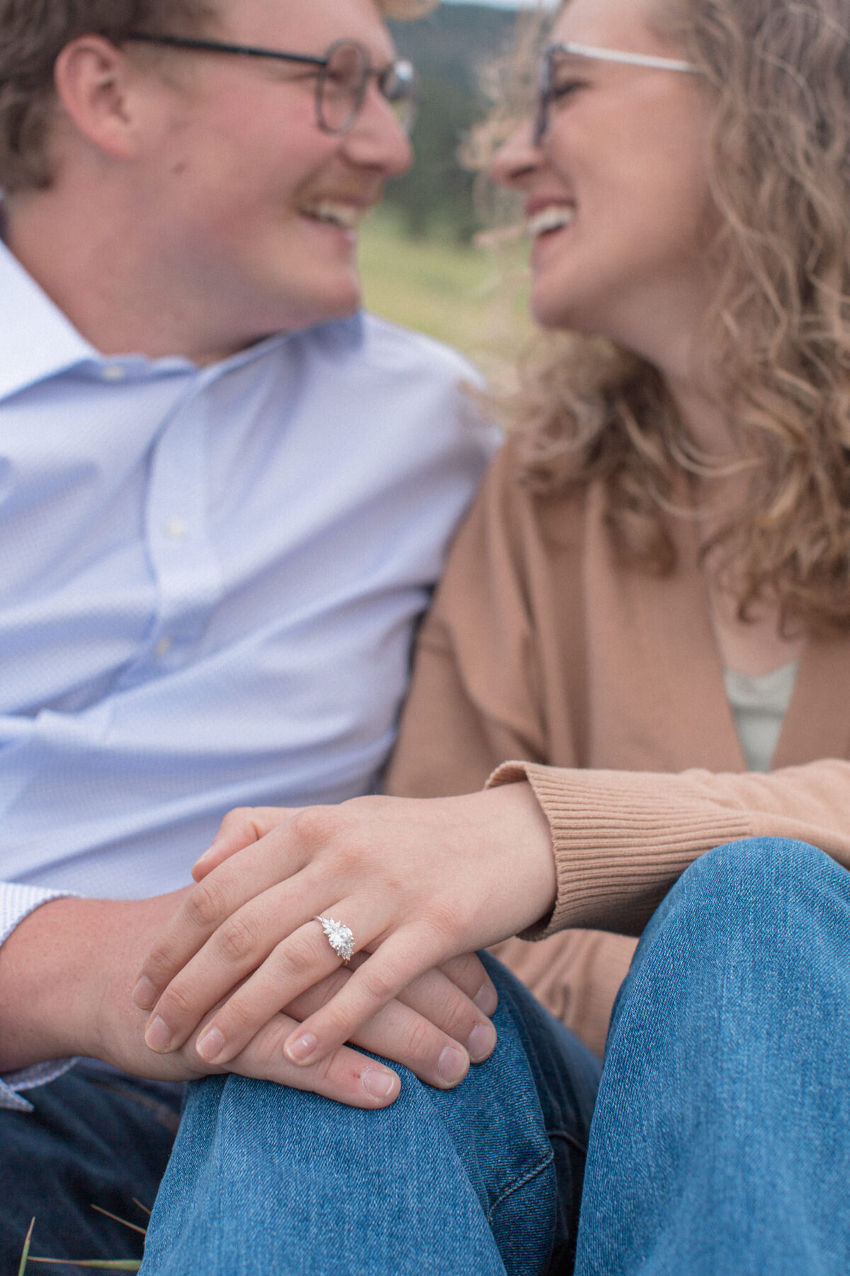 The engagement ring is featured in this photo of  a newly engaged couple smile lovingly at each other at Chautauqua Park in Boulder, Colorado