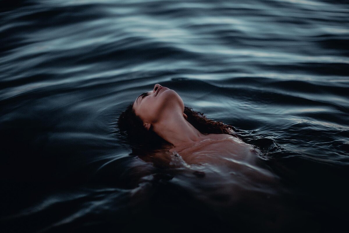 Brunette woman leans back into the water with her face towards the sky under the moonlight