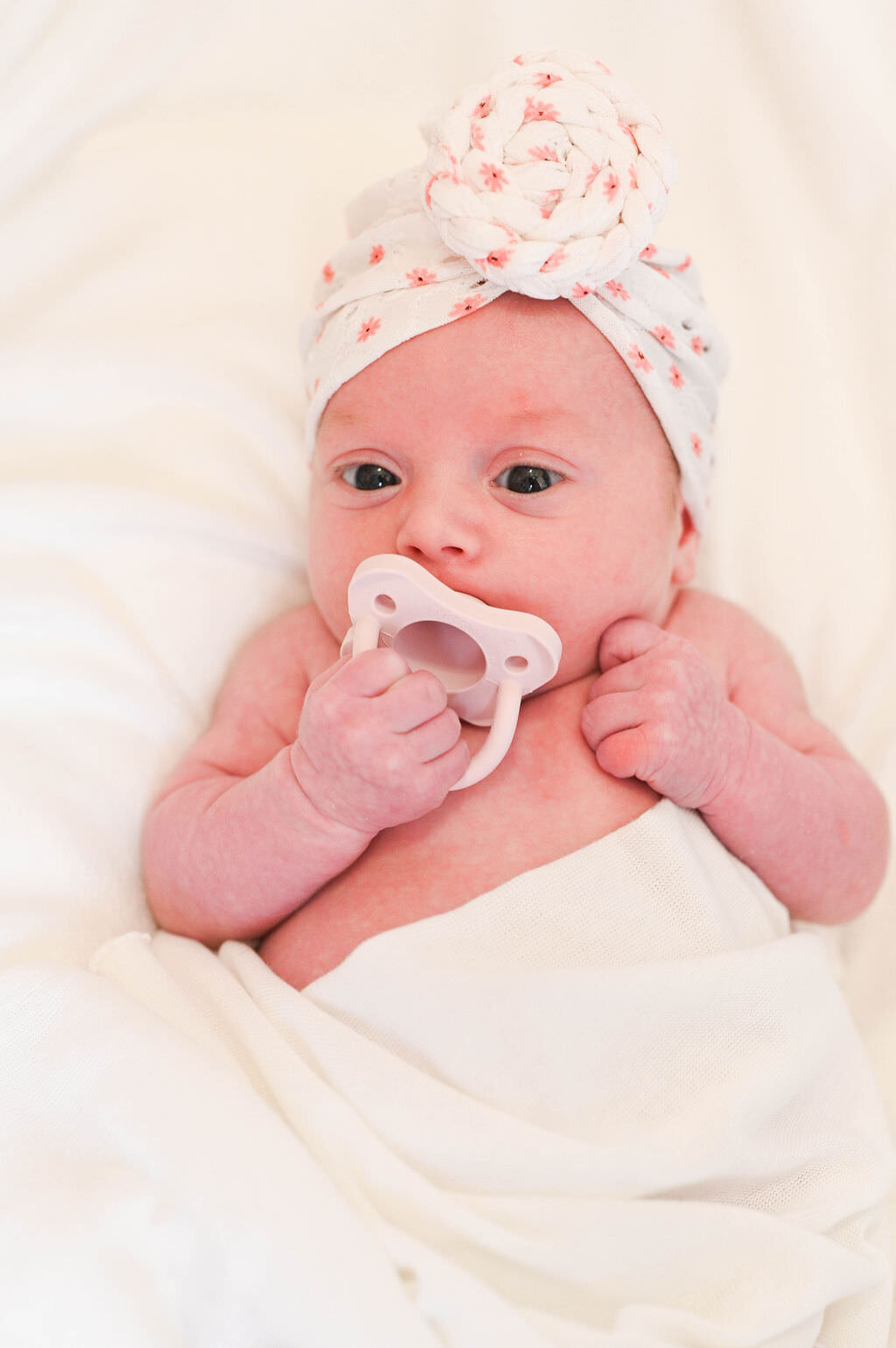A newborn baby sucking on a pacifier.
