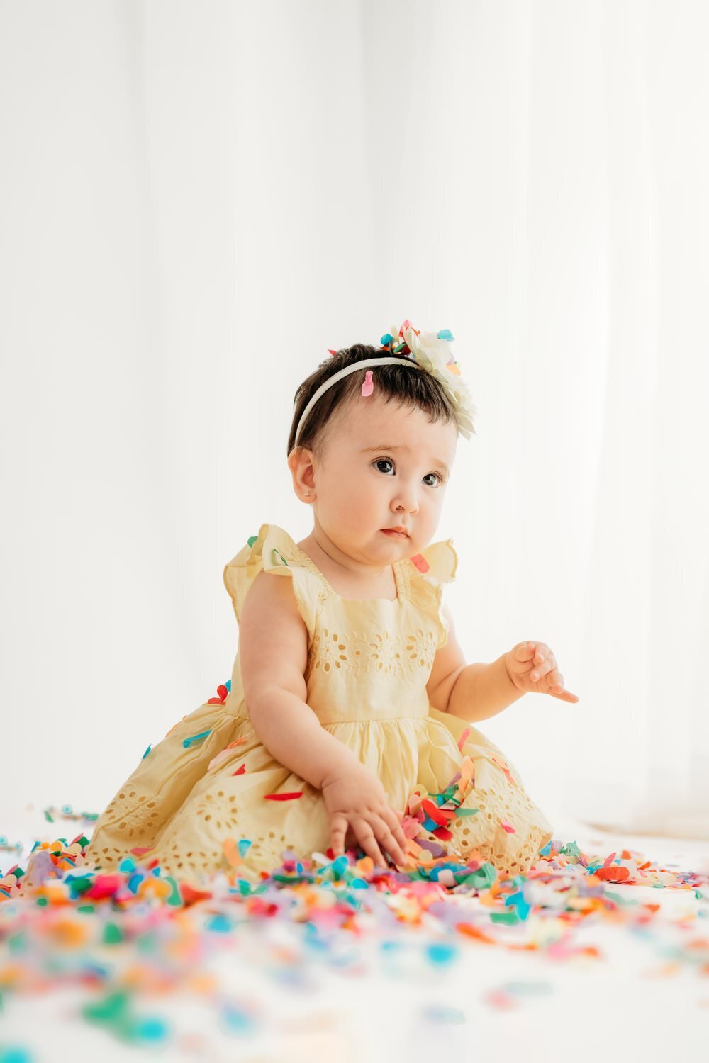 baby calmly plays with rainbow confetti in a studio setting.