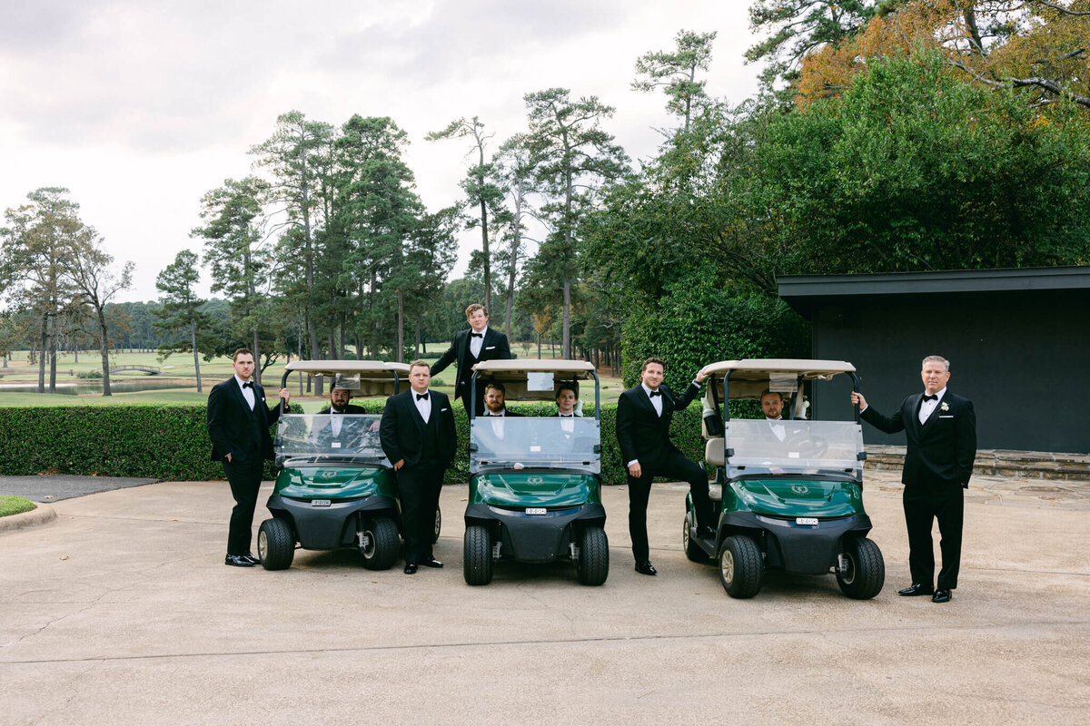 A wedding day photo of the groom and his groomsmen posing with golf carts at the country club