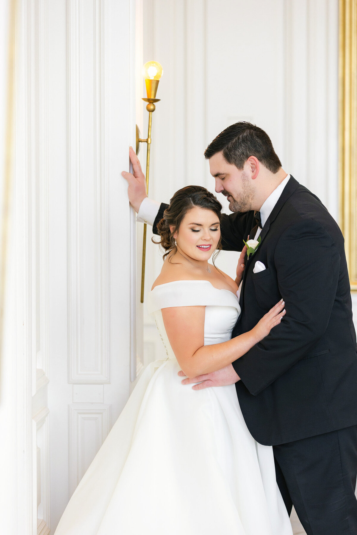 Courtney looking down while Jack leans against the wall in front of her, about to kiss her head, captured in the Governor’s Room at The Adolphus in Dallas in a quiet, intimate wedding portrait.