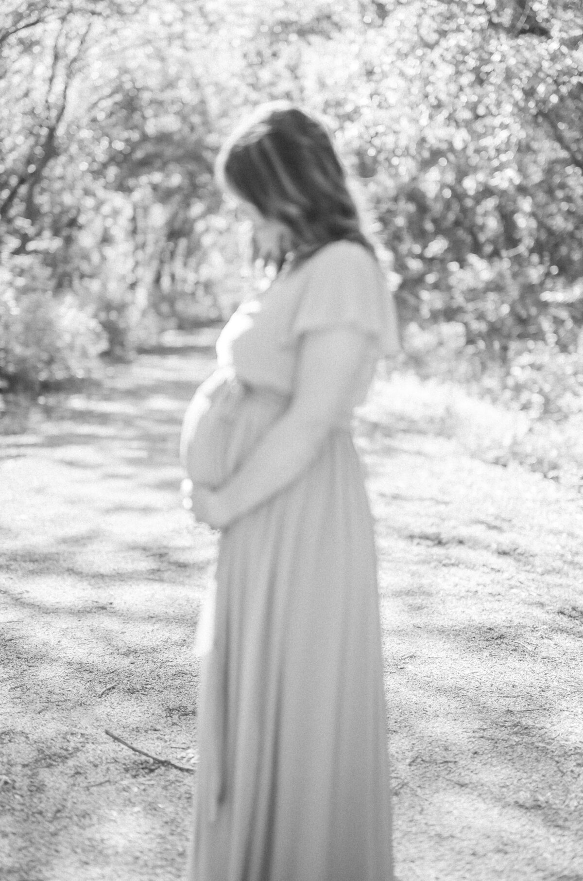 Black and white photo of an expectant mother holding her bump during an outdoor maternity shoot.
