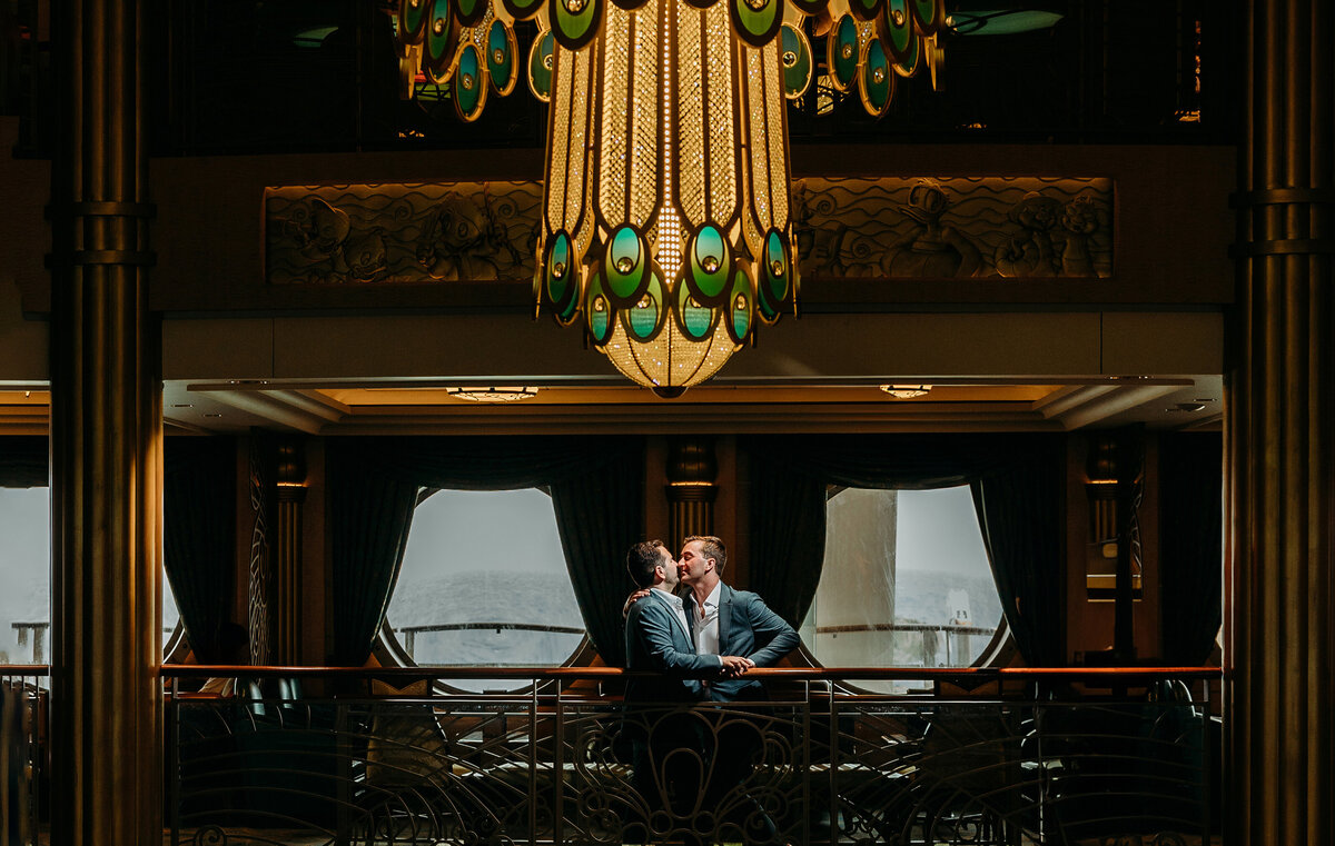 Two grooms share a kiss under the chandelier aboard the Disney Fantasy cruise ship during their destination wedding celebration.