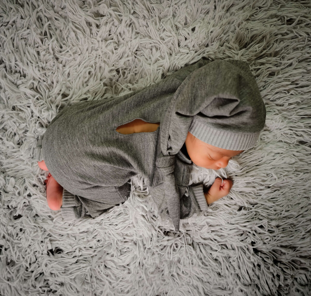 An overhead view of a newborn sleeping on his tummy dressed in a gray outfit and matching hat for his in home newborn session in Kitsap, WA