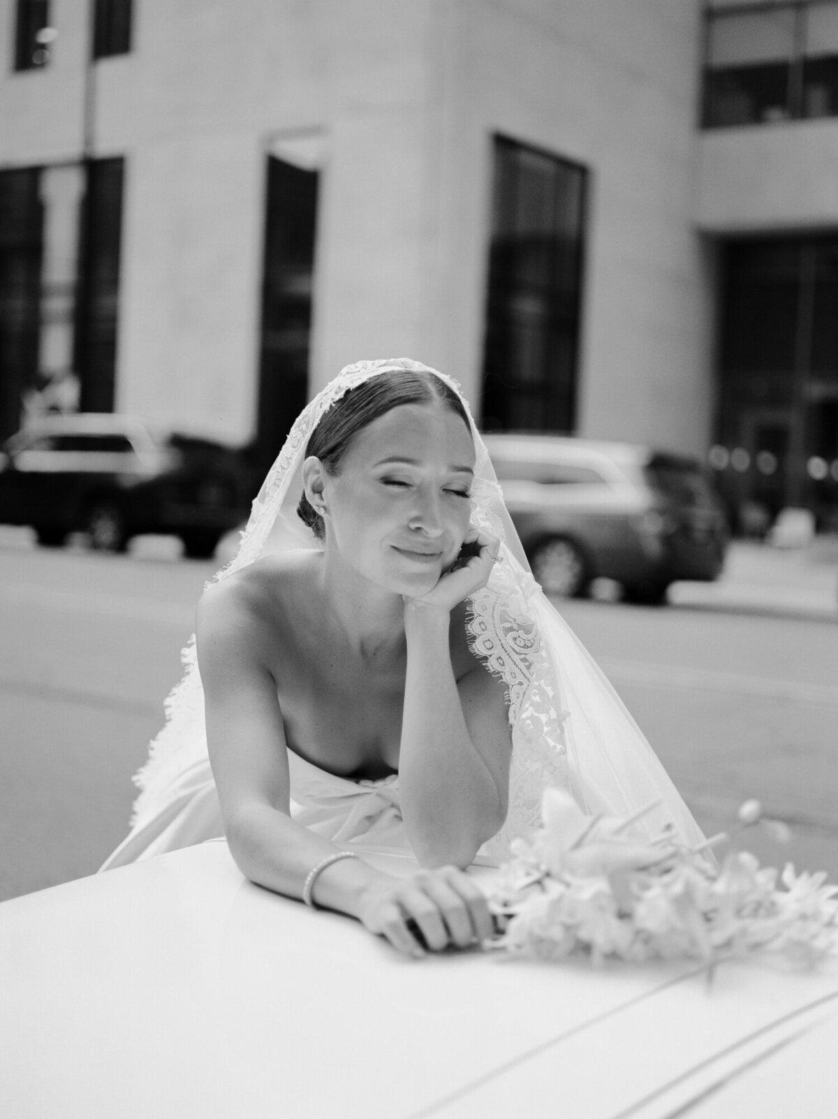 A bride rests peacefully, leaning on a convertible wedding getaway car in Detroit