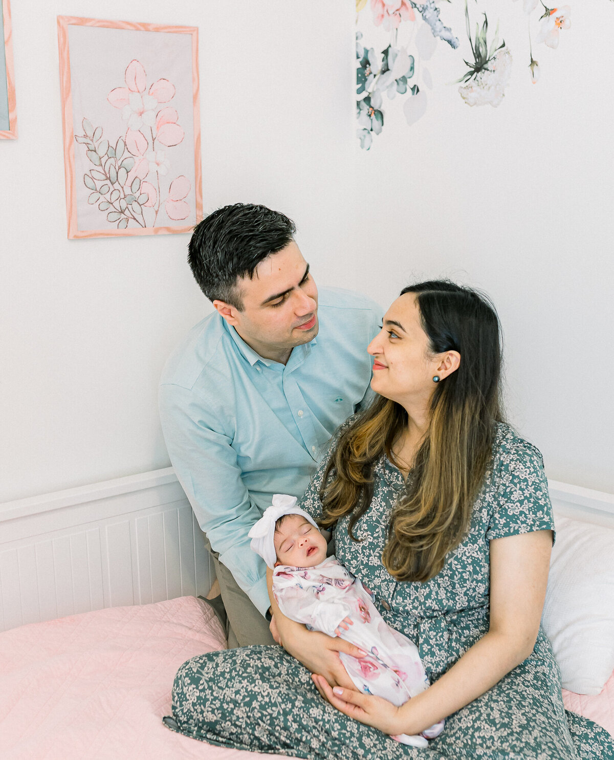Black and white lifestyle newborn photography featuring a loving couple holding their sleeping baby girl. This intimate family moment highlights the joy of welcoming a newborn at home