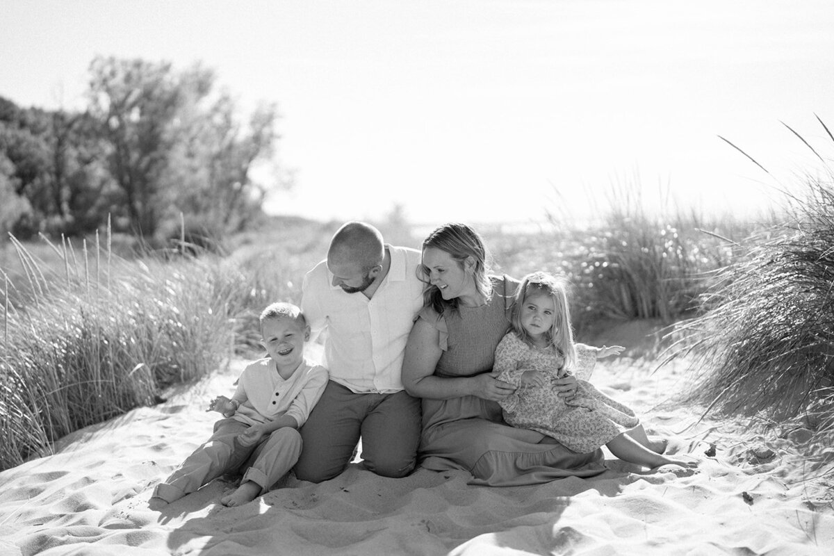 A black and white photo of the Loza family sitting together in the sand at Weko Beach during their family mini session.