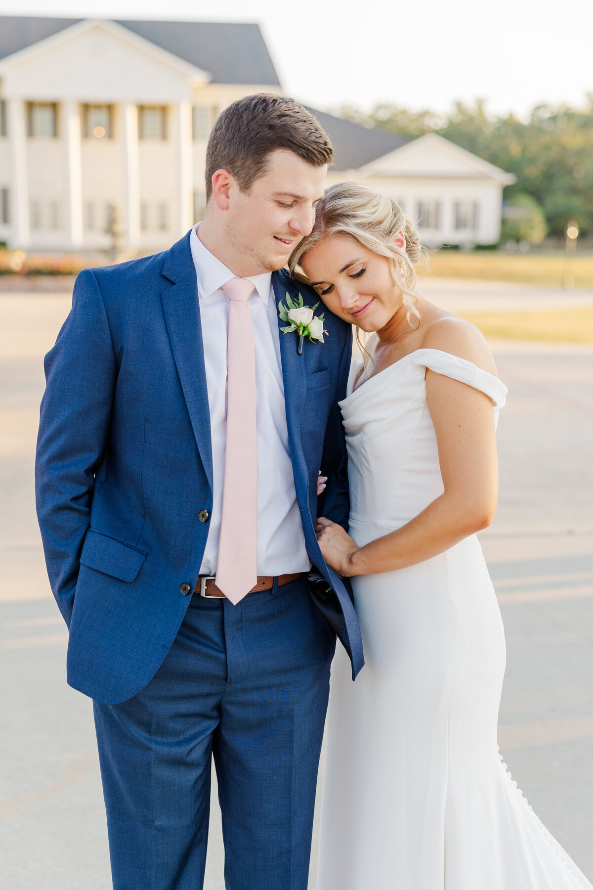 A bride and groom share a tender moment outside a grand southern-style venue at sunset. Captured in Aubrey, Texas, this romantic wedding portrait highlights soft natural light, classic fashion, and refined elegance.