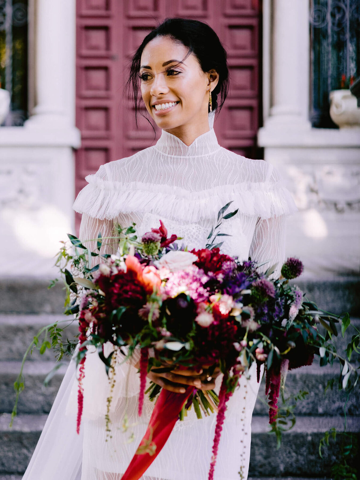 Close-up, half body shot of a bride holding a flower bouquet on a cement stair and wooden door background