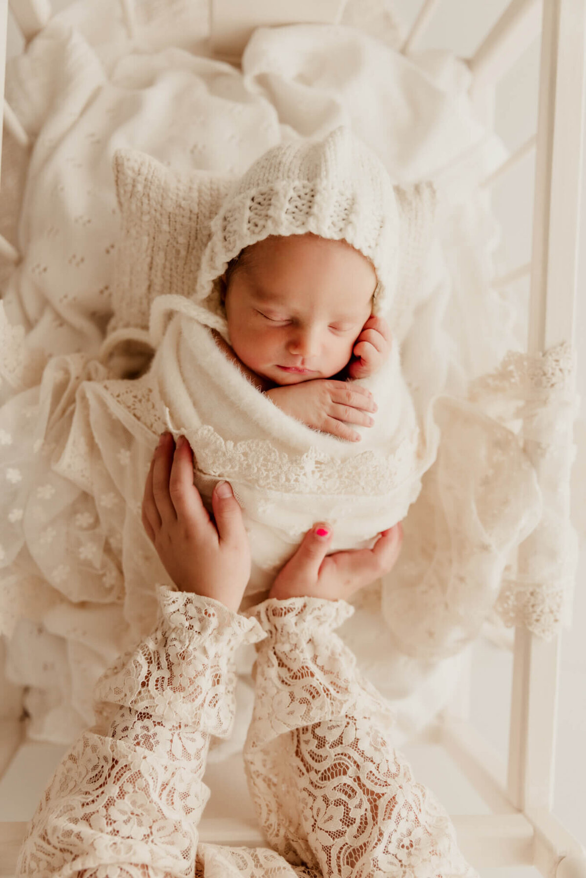 Girl wearing white lace sleeves places her hands on her swaddled baby sister who is sleeping in Oklahoma City.