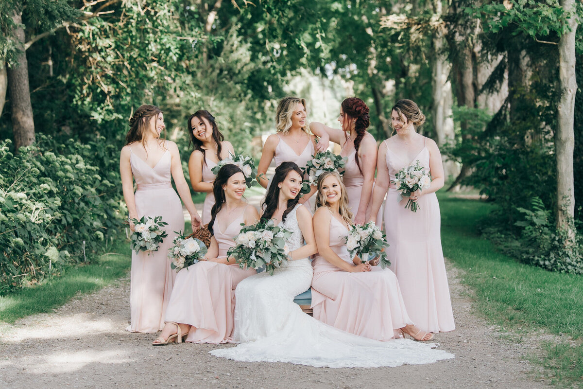 Bride posing with bridesmaids wearing pink bridesmaids dresses in a whimsical forest on a Summer wedding day at Wheatfield Estate