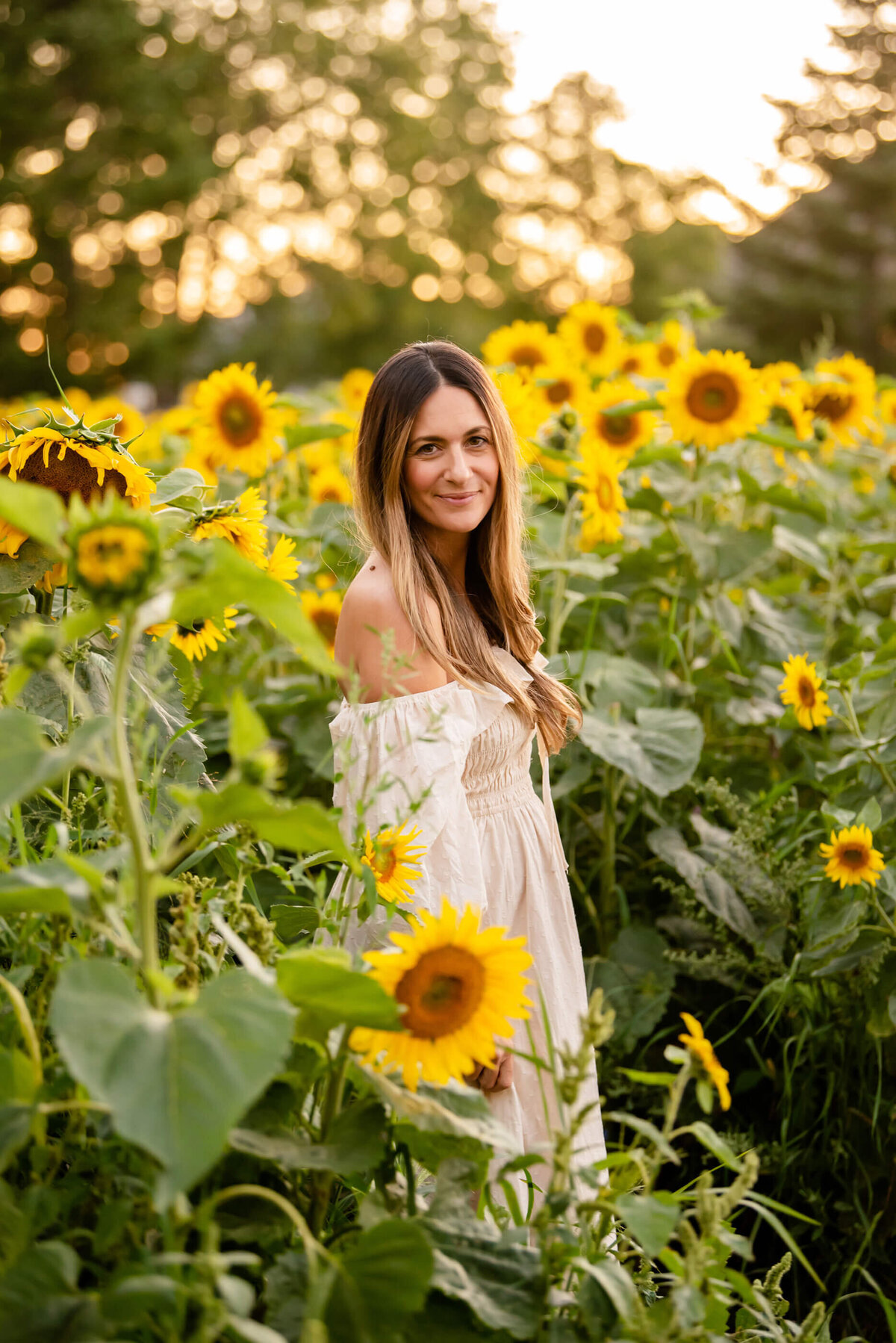 Mom wearing a beige dress standing in a sunflower field for her summer family photos in Burlington, ON