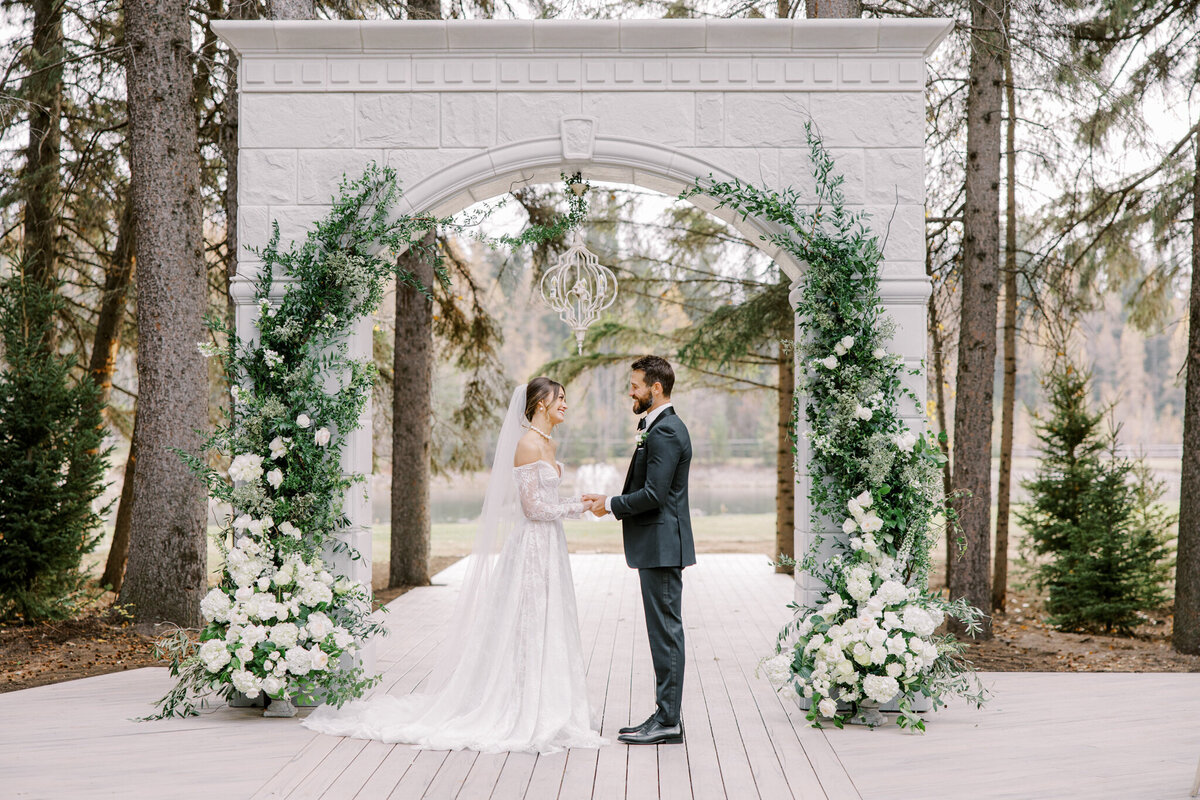 Couple standing at stunning ceremony arch at Archway Manor Weddings & Events, elegant, timeless, European-inspired Red Deer, Alberta wedding venue, featured on the Brontë Bride Vendor Guide.