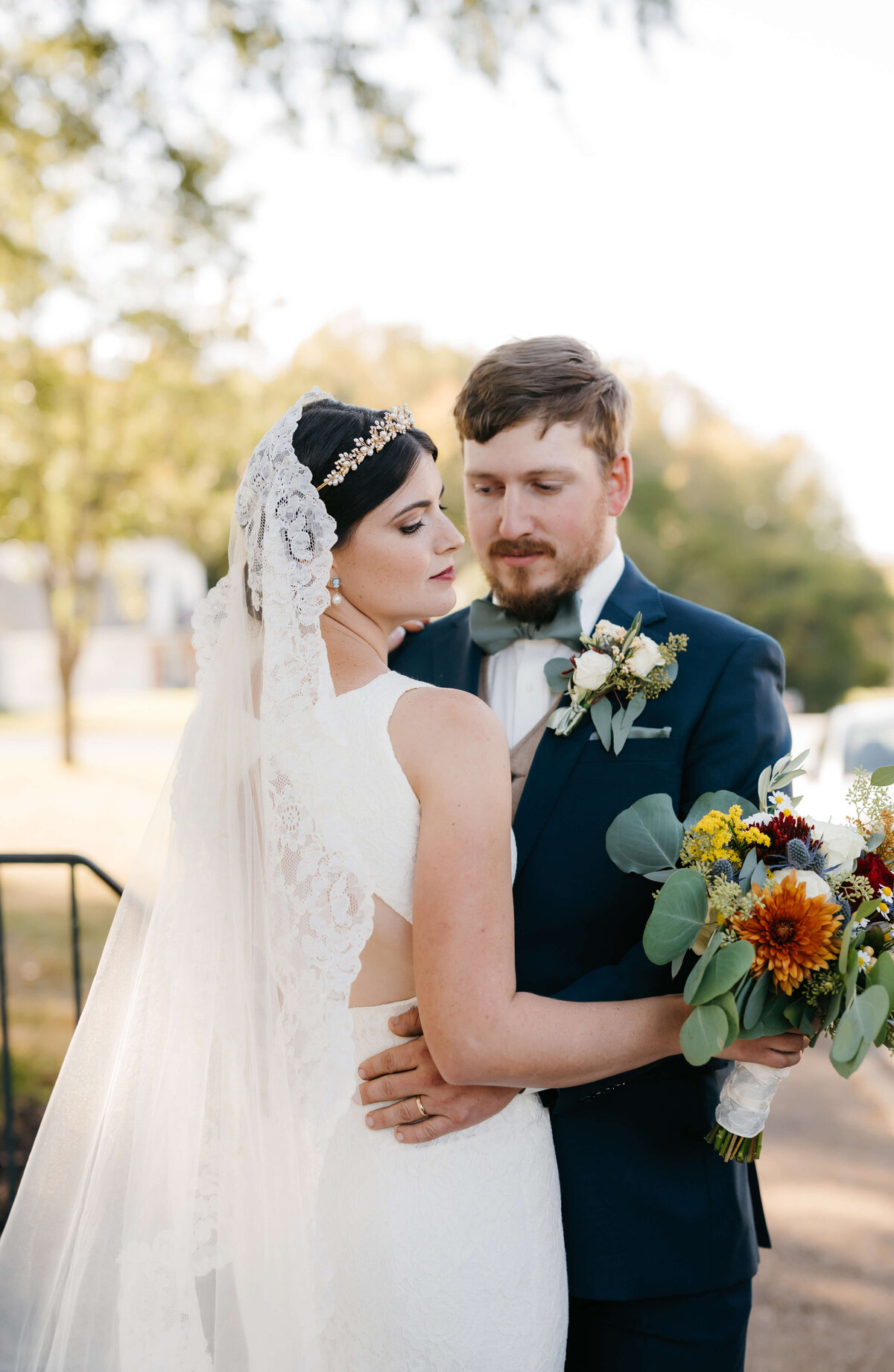 bride in a satin wedding dress and a lace veil is held by her groom who looks to her longingly as she glances down her shoulder for wedding pictures by Virginia wedding photographer