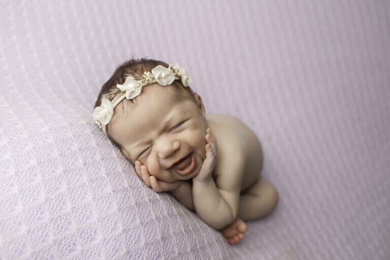 Newborn baby girl posed beautifully with a big, joyful smile, capturing a sweet and heartwarming moment