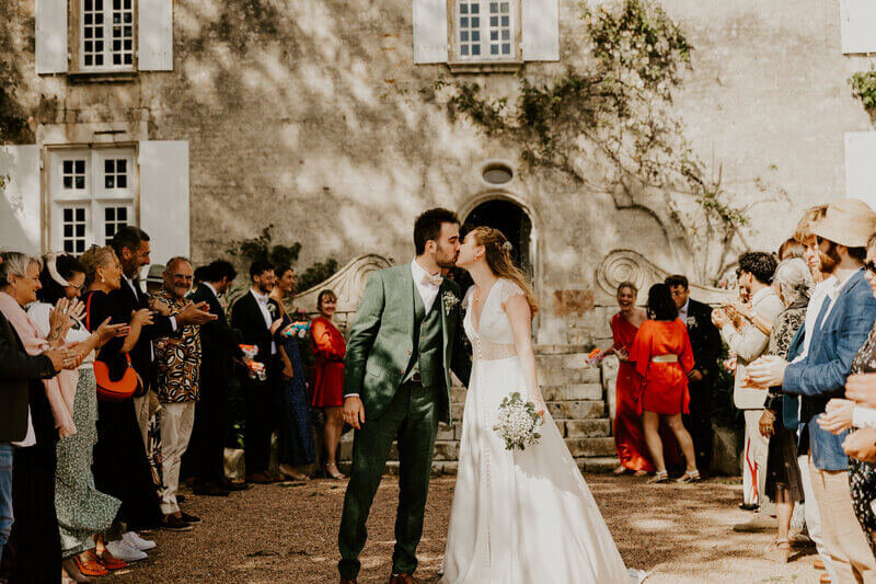 Mariés échangeant un bisous et entourés des invités qui forment une haie d'honneur lors d'une séance photo mariage en vendée.