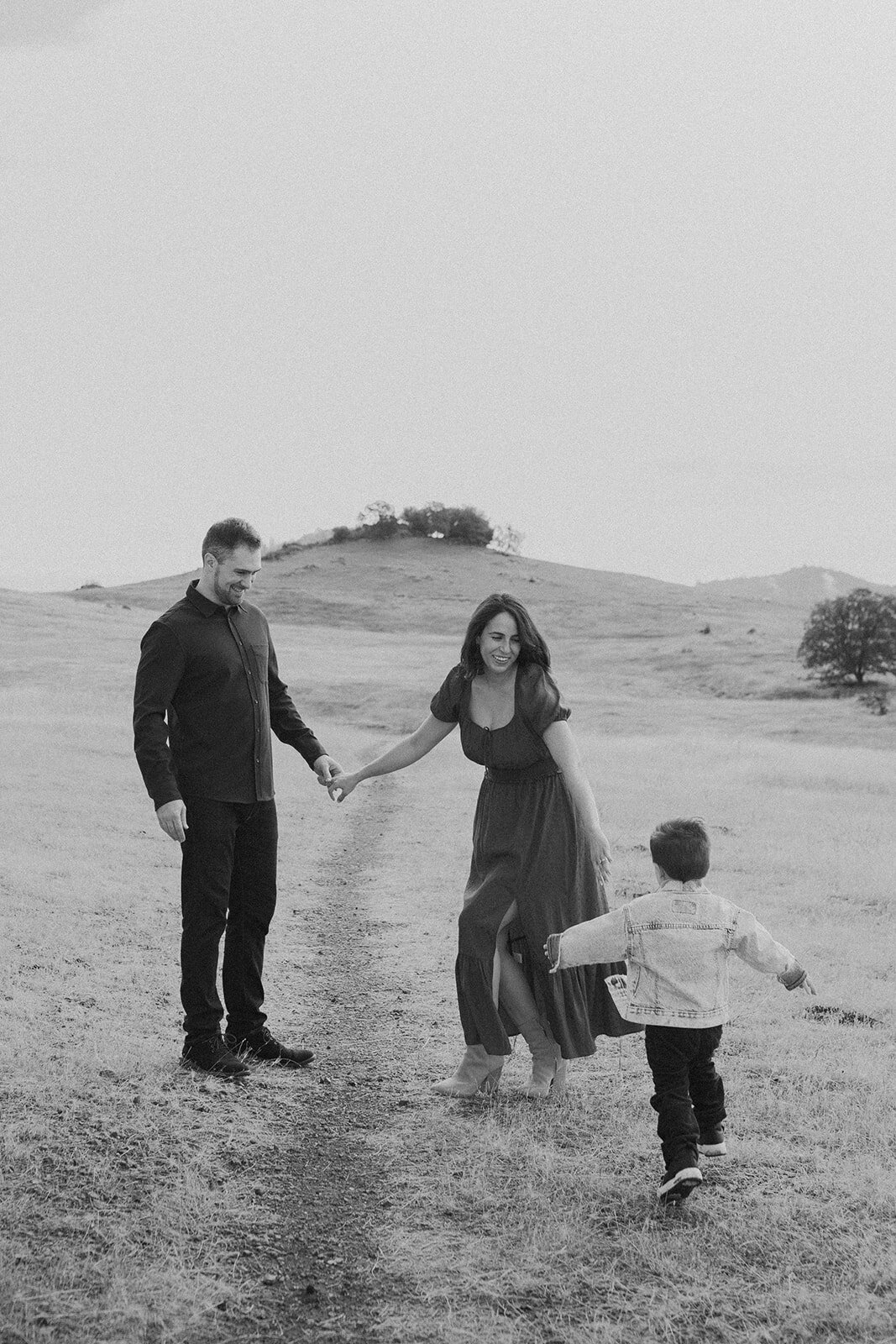 A black-and-white image of a family playing outdoors, captured in a cinematic and documentary wedding photography style.