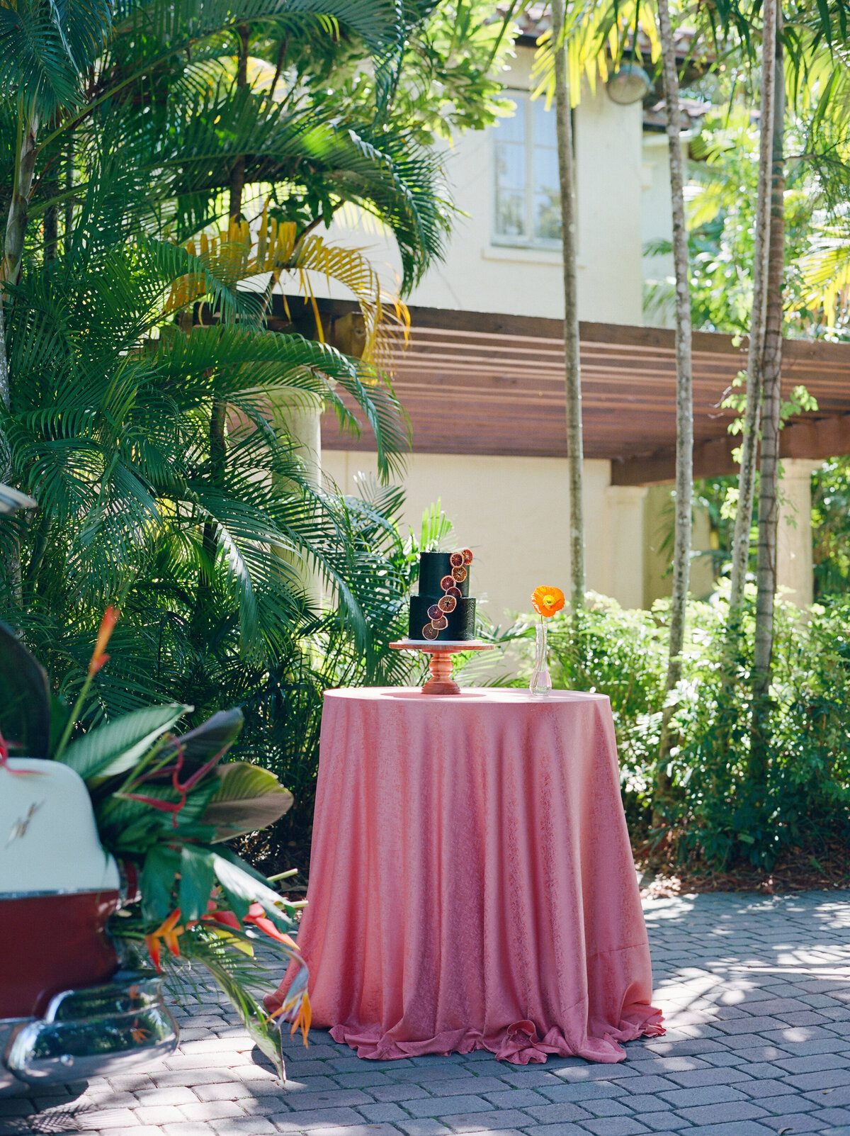 A black cake with orange accents on top of a pinkish red table.