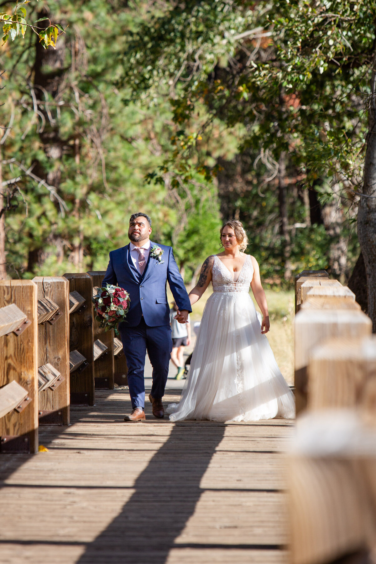 A bride and groom walk along a bridge in Yosemite, California, smiling on their elopement day.