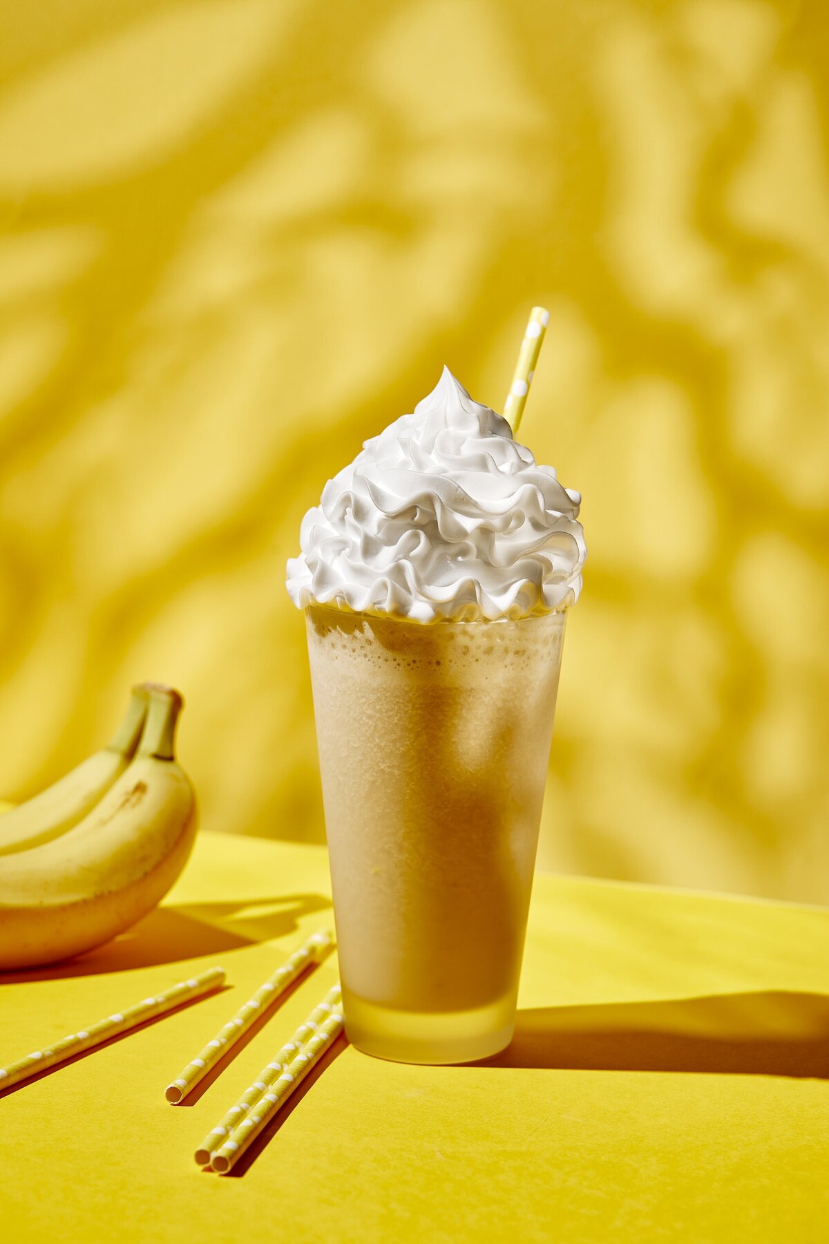 A chocolate banana milkshake topped with whipped cream with bananas next to it.