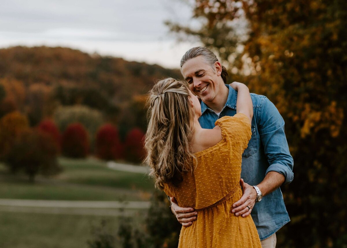 A couple embraces in front of a field during their photo session captured by a Pittsburgh family photographer.
