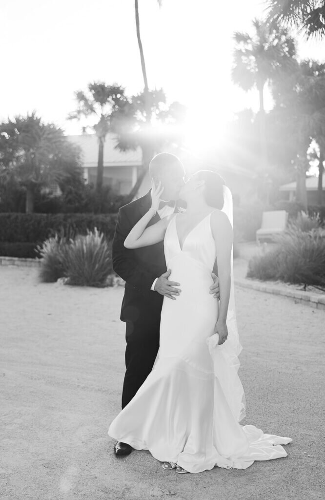 A romantic black-and-white moment as the newlyweds share a kiss at sunset, with golden light streaming through the palm trees. Captured by Claudia Amalia Photography, a Florida Keys wedding photographer specializing in destination wedding photography.